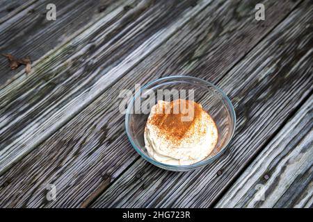 Bananeneis draußen auf der Terrasse oder rustikaler Holztisch im Hintergrund mit Glasschüssel aus hausgemachtem rohem veganem, schönem Creme mit Zimt Stockfoto