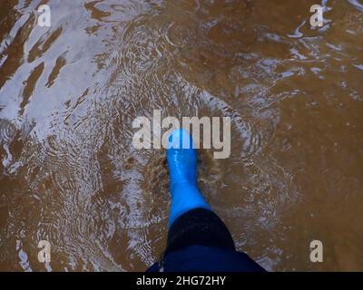 Frühlingslache.Pfütze gehen. Füße in blauen Gummistiefeln im Frühjahr schlammiges Wasser.Schritte im Wasser. Stiefel geht durch die Pfützen. Stockfoto