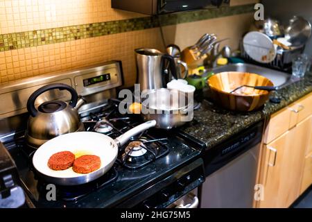 Nahaufnahme von zwei Burger-Patties Kochen auf Keramik-Antihaft-Bratpfanne mit Küche Interieur zeigt Geräte Herd und Geschirrspüler Arbeitsplatten Schränke Stockfoto