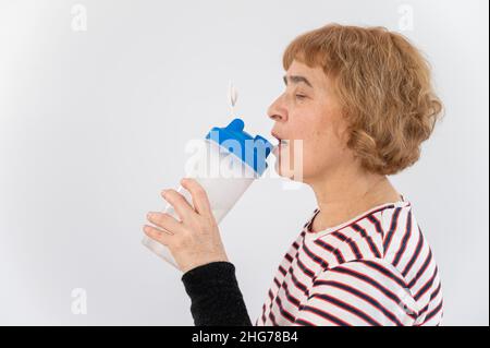 Ältere Frau trinkt Wasser, während sie auf weißem Hintergrund trainiert. Stockfoto