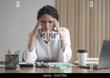 Gestresste Unternehmerin Dame, die unter Kopfschmerzen leidet, die Tempel massiert, während sie im Home Office sitzt Stockfoto