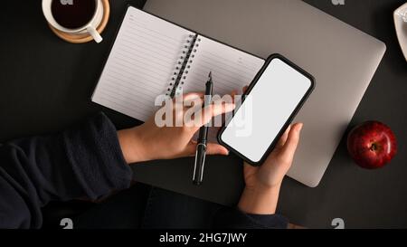 Moderner Hipster-Arbeitsplatz mit einem weißen Smartphone-Display an den Händen der Frau. Draufsicht Stockfoto