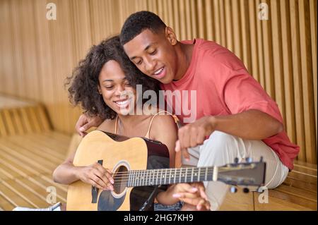 Mann zeigt auf Gitarrensaiten in den Händen der Frau Stockfoto