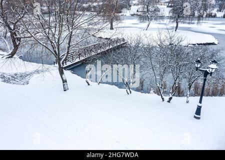 Verschneite Tage im Winterpark mit Holzsteg über dem Wasser. Gefrorene Bäume, bedeckt mit frischem Schnee. Stockfoto