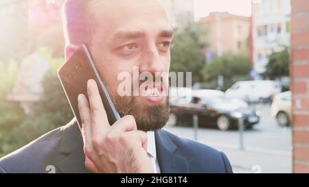 Porträt eines Geschäftsmannes im Anzug, der auf dem Smartphone über das Marketingprojekt mit einem Remote-Manager spricht, der die Unternehmensstrategie plant. Unternehmer Mann vor dem Büro Budilngs stehen. Outdoor-Konzept Stockfoto