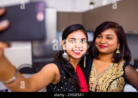 Zwei indische Frauen in Saree sprechen mit der Familie per Telefon Video chatten im Wohnzimmer in zu Hause Stockfoto