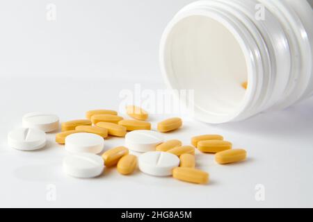 Eine Nahaufnahme von weißen und gelben Pillen fallen aus Die Pillenflasche auf der weißen Oberfläche Stockfoto