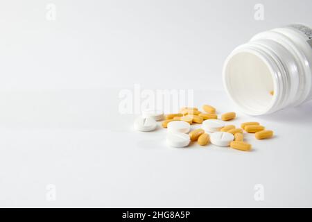 Eine Nahaufnahme von weißen und gelben Pillen fallen aus Die Pillenflasche auf der weißen Oberfläche Stockfoto