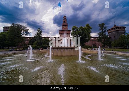 Das Castello Sforzesco, das Schloss von Sforza, das sich an der Piazza Castello befindet, über einem Brunnen gesehen, kommt ein Gewitter. Stockfoto