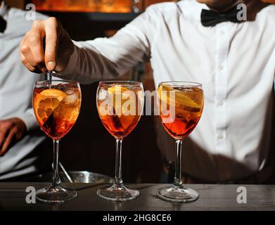 Drei Gläser mit einem aperol Spritz Cocktail sind an der Bar Barkeeper rührt einen Aperitif Stockfoto