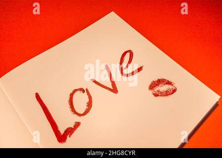 Das Wort Liebe ist in rotem Lippenstift auf Papier geschrieben. Valentinstag. Stockfoto