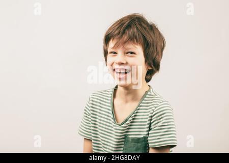 Glücklicher sechs Jahre alter kaukasischer Junge Porträt über grauem Hintergrund. Weißes europäisches Kind lächelt weit und schaut in die Kamera Stockfoto