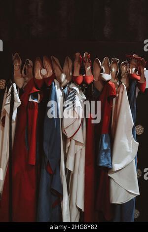 Verschiedene Mode-Outfits und High Heels Schuhe hängen in einer Reihe im Backstage-Bereich. Vertikale Modeaufnahme Stockfoto