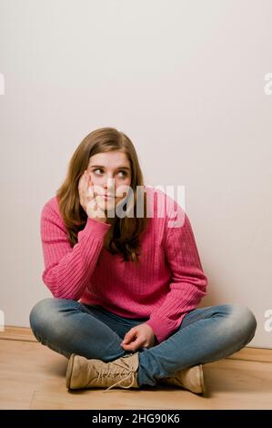 Brunette Tween Mädchen in einem rosa Pullover auf dem Boden sitzen Stockfoto