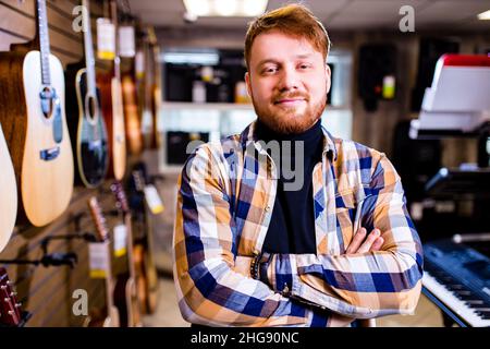 Ein Mann mit rotem Ingwer-Haar und Beatd zieht eine Gitarre in einem Musikgeschäft in Betracht Stockfoto