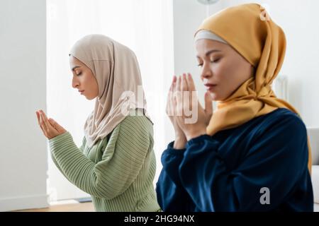 Junge arabische Frau betet in der Nähe verschwommen asiatische Mutter zu Hause Stockfoto