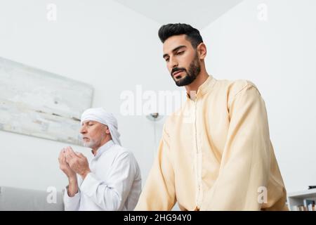 Niedrige Ansicht des bärtigen arabischen Mannes nahe reifem Vater, der zu Hause betet Stockfoto
