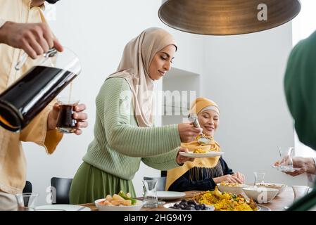 Arabische Frau serviert Pilaf, während Ehemann Tee und interracial Familie zu Hause gießt Stockfoto