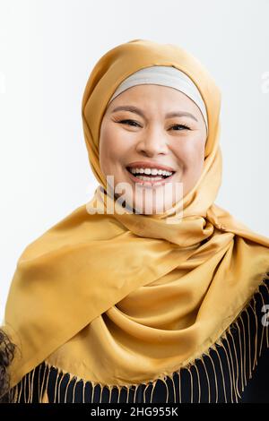 Glückliche asiatische muslimische Frau in Hijab lächelt an der Kamera isoliert auf weiß Stockfoto