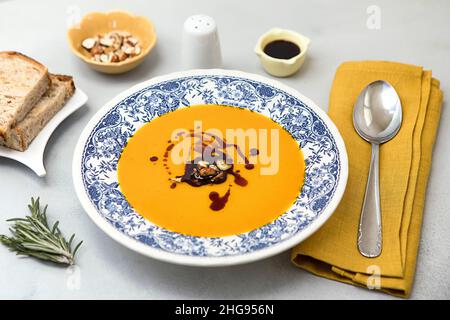 Frische Kürbiscremesuppe auf dem Teller mit Haselnüssen und Kürbisöl, serviert mit frischem Brot. Bereit, Butternut-Kürbissuppe auf neutralem Backgrou zu essen Stockfoto