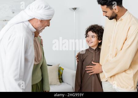Reifer muslimischer Mann umarmt Tochter, während er zu Hause einen arabischen Enkel anschaut Stockfoto