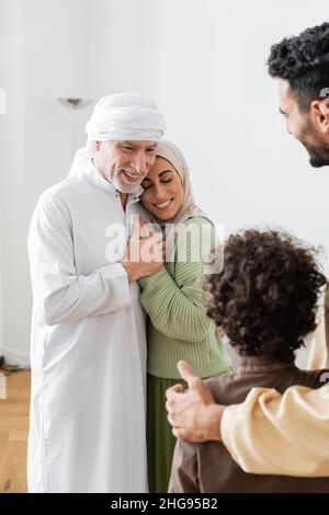 Zufriedener muslimischer Mann umarmt arabische Tochter in der Nähe verschwommene Familie Stockfoto