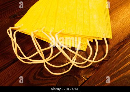 Gelbe medizinische Einweg-Gesichtsmasken auf einem braunen Holztisch. Viele chirurgische 3-lagige Masken auf einem wunderschönen strukturierten Holzhintergrund. Hygiene Stockfoto