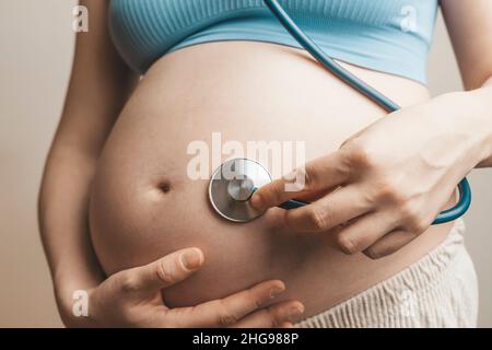 Eine Schwangere hört dem Herzschlag des Babys und den Bewegungen mit einem Stethoskop oder Fetoskop oder Pinard Horn zu. Pränatale fetale Gesundheit, Angst, Angst Konzept. Hochwertige Fotos Stockfoto