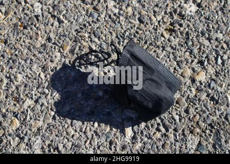 Nahaufnahme einer schwarzen Maske zur Verhinderung der Ausbreitung des Covid-19-Virus, das auf dem Asphalt liegt Stockfoto