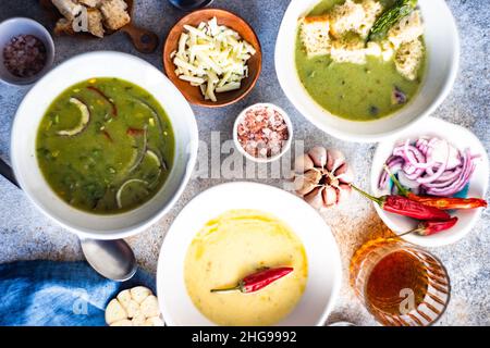 Blick von oben auf drei Schalen mit cremig-würziger Spinatsuppe und Blumenkohlensuppe mit Croutons und einem Glas Wein Stockfoto