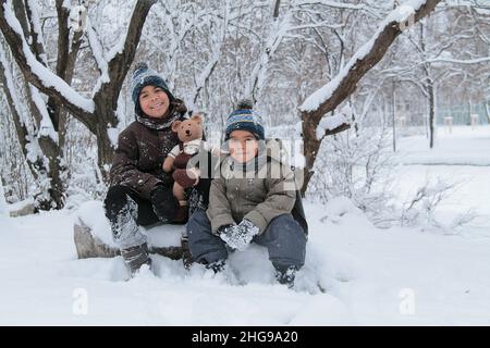 Portrait von zwei Jungen, die mit ihrem Teddybären im Schnee sitzen, Bulgarien Stockfoto