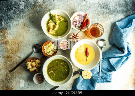 Blick von oben auf drei Schalen mit cremig-würziger Spinatsuppe und Blumenkohlensuppe mit Croutons und einem Glas Wein Stockfoto