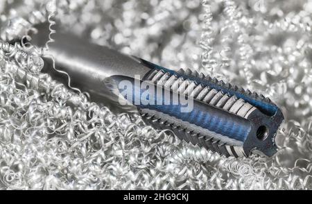 Spiralspitze gerader, geriffelter Hahn in einem Metallspan-Haufen. Schöne Stahl Gewindebohrer Detail. Bohrer mit metrischem Schraubgewinde zum Erstellen von Gewindebohrungen. Stockfoto