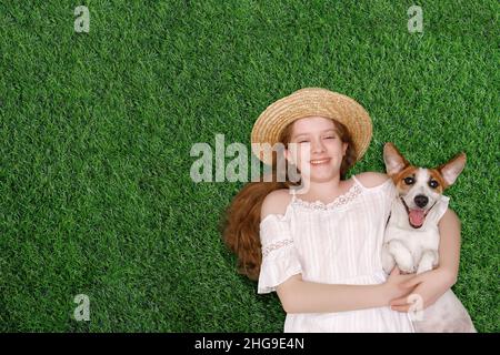 Nettes Mädchen und Hund genießen den Frühlingstag auf dem Rasen im Park. Stockfoto