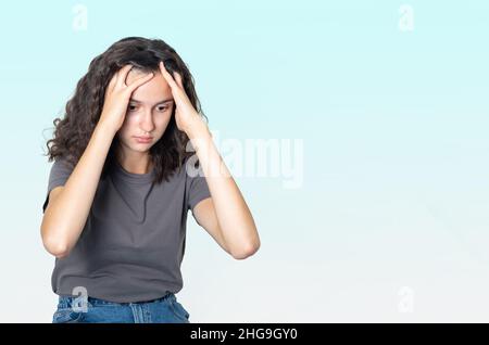 Konzept der psychischen Gesundheit. Verärgert trauriges Teenager-Mädchen, das unter Einsamkeit leidet und ihren Kopf mit den Händen auf einem blauen Hintergrund hält, Platz kopieren. U Stockfoto