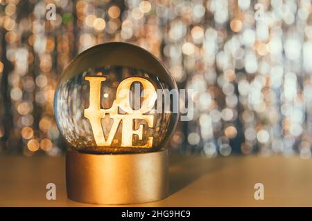 Valentinstag Hintergrund. Glitzer-Globus mit WORTLIEBE auf dem goldglänzenden Bokeh-Hintergrund. Selektiver Fokus. Speicherplatz kopieren Stockfoto