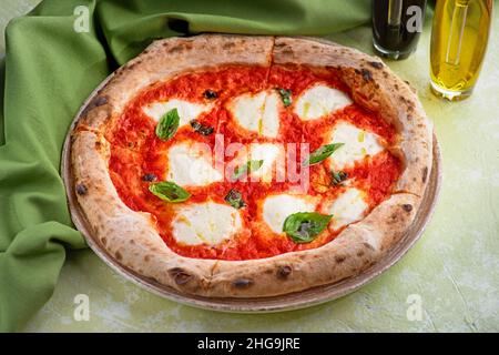 Italienische Pizza mit Tomate und geschmolzenem Goldkäse, Kräutern und Basilikum auf dem hellen Tisch. Konzept der gesunden Ernährung für das Menü. Stockfoto
