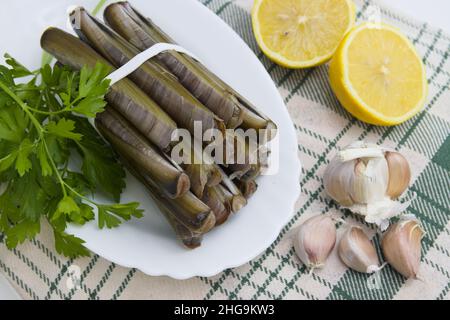 Tisch, in dem es lebende Rasiermuscheln (ensis) zusammen mit Zitrone und Knoblauch gibt, um eine Vorspeise vorzubereiten Stockfoto