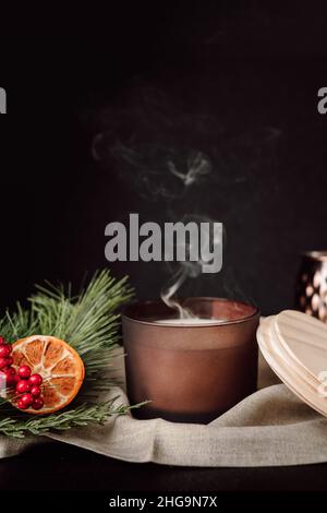 Stillleben Zu Weihnachten. Schokolade braune Kerze mit Rauch gegen Dunkel Hintergrund mit getrockneten Orangen und Cranberries. Moody Spa Stillleben. Stockfoto