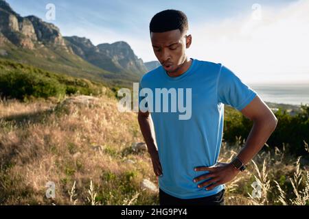 Schwarzer junger Erwachsener, der sich auf seinem Trail Run in den Berg den Atem raubt Stockfoto