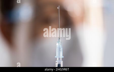 Medizinische Nahaufnahme-Spritze mit einem Impfstoff gegen Covid-19-Coronavirus, Grippe und medizinisches Fachpersonal im Hintergrund Stockfoto