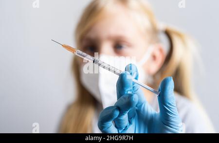 Medizinische Nahaufnahme-Spritze in der Hand der Ärzte mit Impfstoff gegen Covid-19-Coronavirus, Grippe und blondes Kind im Hintergrund Stockfoto