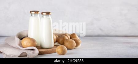 Vegane Milch auf pflanzlicher Basis in zwei Glasflaschen. Alternative Kartoffelmilch und Kartoffelknollen auf grauem Tisch Stockfoto