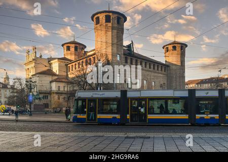 Eine Straßenbahn, die vor Casaforte von Acaja und dem Palazzo Madama auf dem Piazza Castello Platz bei Sonnenuntergang, Turin, Piemont, Italien, vorbeifährt Stockfoto