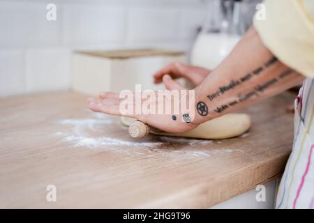 Beschnittene Ansicht von tätowierten reifen Mann rollenden Teig mit Nadel in der Küche Stockfoto