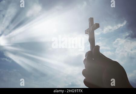 Hand hält das Heilige Kreuz mit strahlender Sonne. Christentum Konzept. Stockfoto