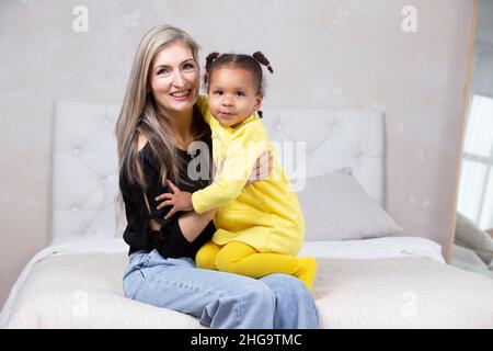 Multiethnische Mutter und Tochter. Fröhliche Mutter umarmt ihre Tochter afrikanischer Nationalität. Familie aus verschiedenen Rassen. Stockfoto