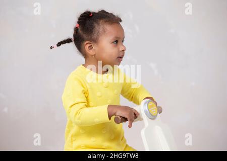 Kleines afroamerikanisches Mädchen in gelbem Kleid mit lockigen Zöpfen auf hellem Hintergrund. Stockfoto