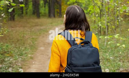 Frau mit Rucksack in orangefarbenem Pullover geht durch den Wald Stockfoto