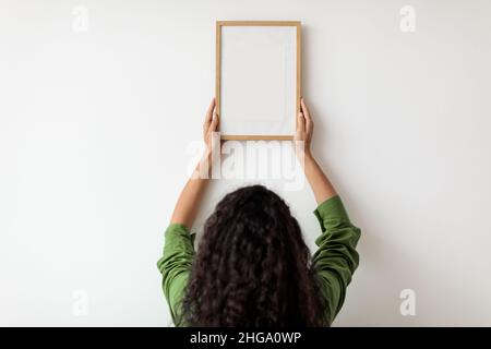 Rückansicht Der Dame, Die Den Bilderrahmen An Der Innenwand Aufgehängt Hat Stockfoto